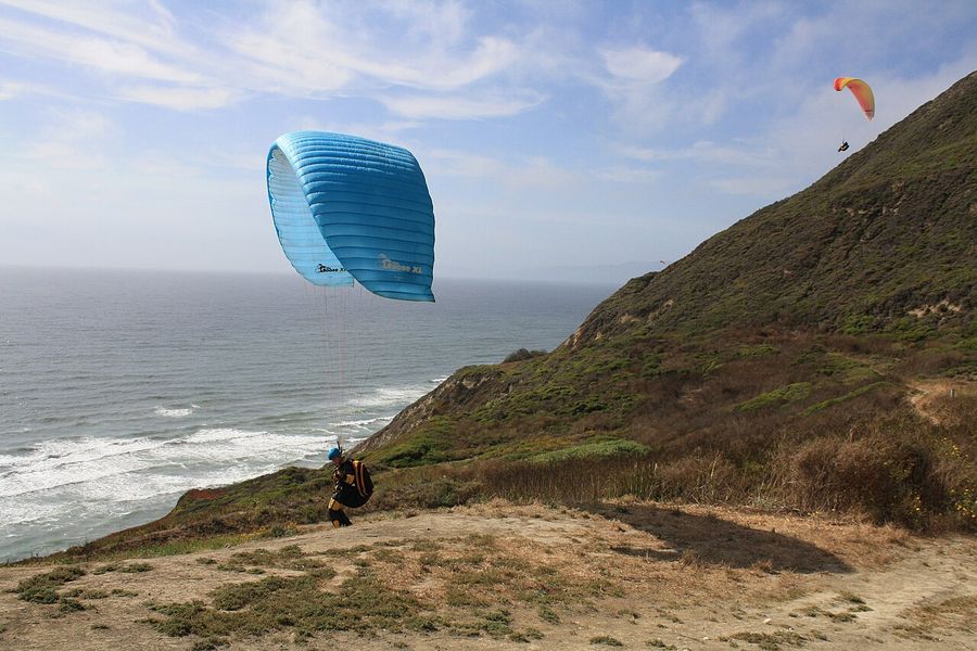 A paraglider soaring the green face of Mussel Rock above the beach